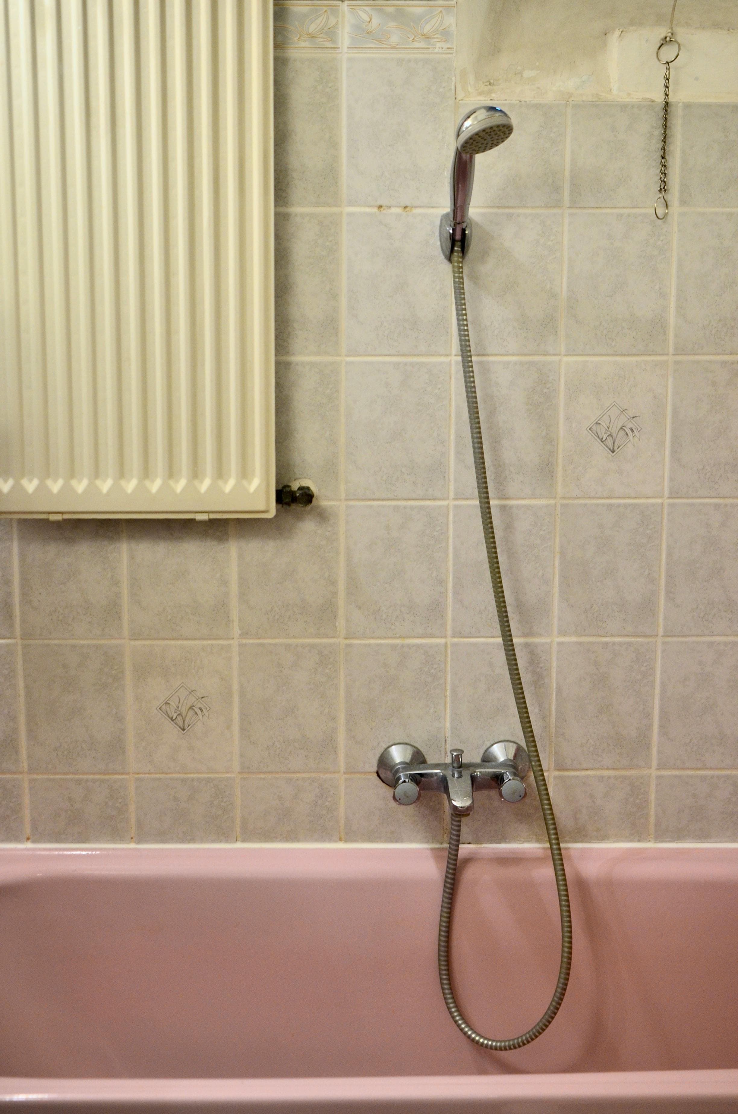 A modern shower head spraying water against a tiled bathroom wall